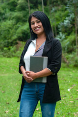 Fototapeta premium Smiling south american teacher holding a book in a green park