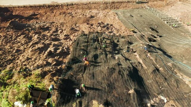 Protection of road from mountain slough, rockfall with metal accumulative restraining net fences. Workers constructing anti-landslide concrete wall prevent protect against rock slides. Rockfall