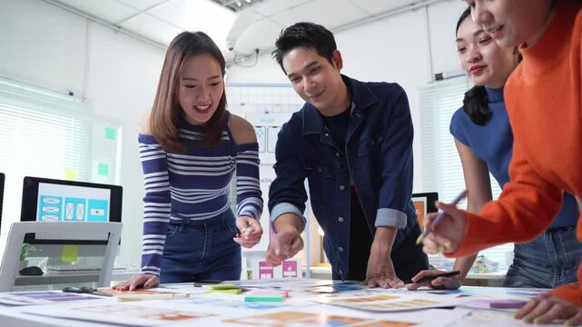Young asian designers discussing and planning a new project together in a modern office using colorful sticky notes on a large sheet of paper