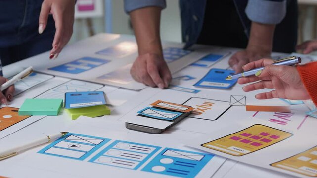 Software engineers collaborating on mobile application design, developing user interface and user experience through paper prototyping with smartphone at creative workspace