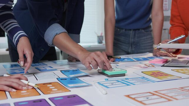 Professional UXUI designers collaborating and arranging paper prototypes of mobile application, working together at shared table during creative design process
