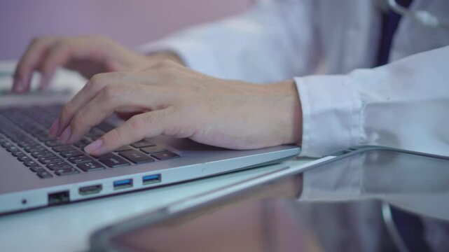 Close up of Asian male doctor&rsquo;s hands typing on laptop in hospital office. Medical professional working at desk, using technology for healthcare documentation and clinical tasks.