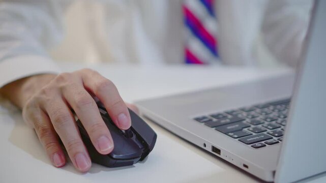 Close up of businessman&rsquo;s hand clicking and moving a computer mouse. Man in formal shirt and tie working at desk. Professional office setting, tech usage, and modern business concept in detail.