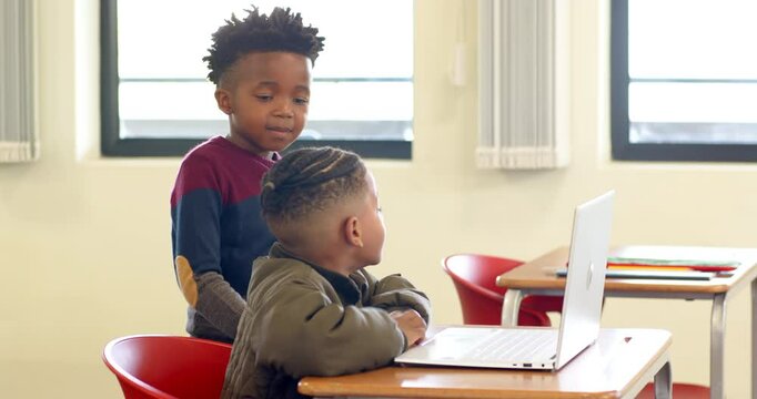 In school, young african american boy pointing at laptop, helping classmate with assignment