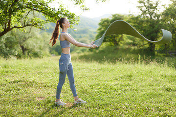Young woman practicing outdoor fitness with resistance band in a green, grassy field, showcasing...