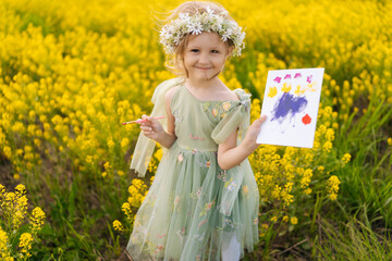 Portrait of cute talented child girl wearing flower crown and beautiful dress showing painting...