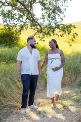 On a warm summer day, a joyful pregnant couple enjoys nature, cherishing their love and the upcoming arrival of their baby, soaking in the gentle sunlight filtering through the greenery