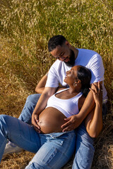 An African American couple enjoys a beautiful summer moment together. The husband lovingly embraces his pregnant wifes belly, filled with love and anticipation for their growing family