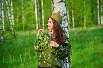 A woman in military uniform is standing in the forest. She is wearing a camouflage jacket. The concept is calm and serenity, as the woman is surrounded by nature.