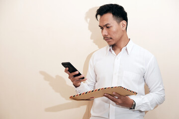 A Southeast Asian man smiling and wearing employee suit holding a brown envelope containing his...