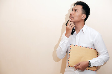 A Southeast Asian man smiling and wearing employee suit holding a brown envelope containing his...