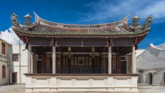 The building of the ancient Chinese theater. A scene with columns. Tiled roof with curved cornice edges and figures of mythical creatures, dragons above. Decorative carved ornaments. Malaysia. Penang.