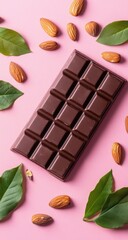 Dark chocolate bar surrounded by almonds and leaves on a pink surface