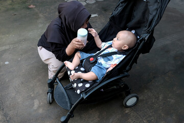 Young woman muslim with a cute baby boy in baby stroller at outdoor in the morning, happy family