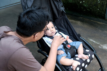 A southeast asian man with a cute baby boy in baby stroller at outdoor in the morning, happy family