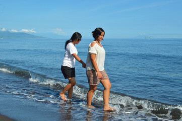 Teenage girls walk side by side, feeling the bubbly sea foam under their feet while enjoying the tropical beach scenery.