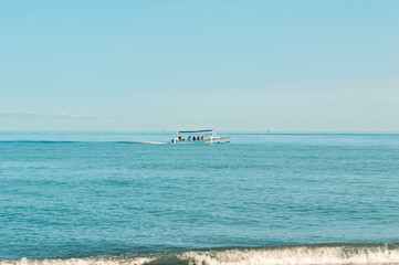A traditional fishing boat glides across the tranquil turquoise sea near the beach, leaving a trail in the peaceful waters.