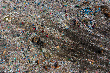 Aerial view of a vast, sprawling landfill with a bulldozer compacting waste and animals scavenging,...