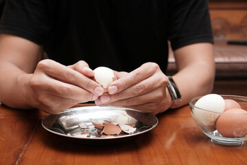 Close up of a man's hands peeling chicken boiled egg  on the kitchen table, prepares breakfast at home, health care and food concept. Copy space