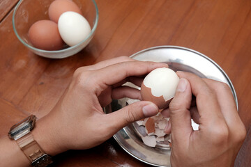 Close up of a man's hands peeling chicken boiled egg  on the kitchen table, prepares breakfast at home, health care and food concept. Copy space