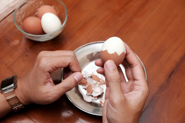 Close up of a man's hands peeling chicken boiled egg  on the kitchen table, prepares breakfast at home, health care and food concept. Copy space