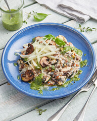 Oat risotto with vegetables, mushrooms and green pesto on blue plate
