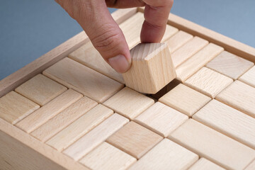 A hand placing a wooden block into a box of neatly arranged pieces, symbolizing organization,...