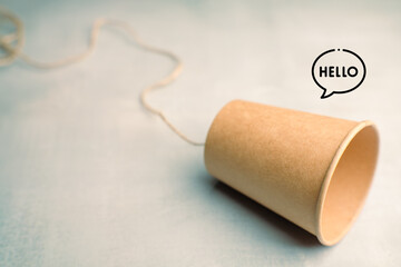 A brown paper cup connected by string with the word “HELLO” in a speech bubble. A playful and creative symbol of communication, connection, and friendly conversation