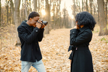 Black man take a photo of black woman in autumn park