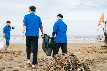 Group of volunteers cleaning the beach while wearing blue shirts and gloves during a cloudy day