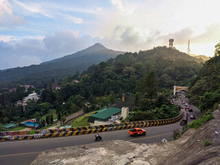 Winding mountain road of Puncak Pass in Bogor cuts through lush green hills with scenic views of...