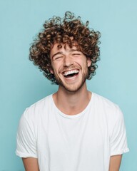 Authentic young man with curly hair laughing in white t-shirt against light blue background, natural joy, modern lifestyle and positive energy concept