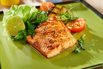 Salmon steak with grilled vegetables, bright lighting, overhead green plate composition