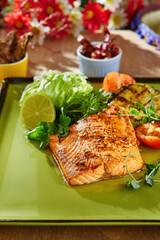 Salmon steak on green plate, bright natural lighting, overhead composition with grilled vegetables