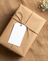Kraft Paper Gift Box with Blank Label on Burlap Background.photo, commercial, eco, elegant, graphic, image, label, marketing, minimal, present, ribbon, sustainable, warm, branding,