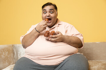 Overweight indian man eating gulab jamun sweets. Fat guy enjoy delicious food dessert - Concept of diabetes, healthcare, obesity. Addiction.