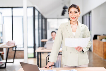 Female leader with a smile standing in the office and her team in the background. a woman boss and corporate business people at work