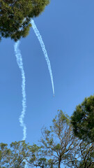 Jet plane with smoke trail flying over trees on clear blue sky