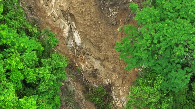 Drone view of a hillside landslide during heavy rain, with mudslide and debris clearing forest vegetation, demonstrating how torrential rainfall destabilizes slopes and damages nature. Thailand.
