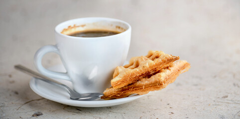 A cup of coffee and a waffle on a saucer.