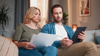 Colleagues sitting on couch and having discussion. Man and woman sitting on sofa. Male and female working on business project. Woman holding work papers. Business partners using tablet.
