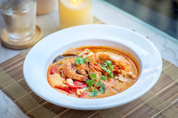A bowl of Tom Yum soup with shrimp, vegetables, and spices.