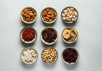 Assorted nuts and dried fruits in ceramic bowls on gray background
