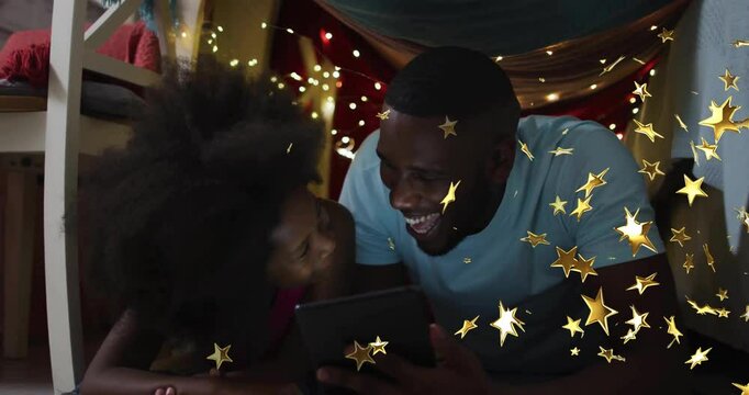 Father nudging daughter tablet tap in blanket fort, generating animated stars highlighting edtech