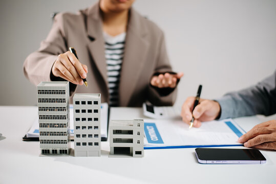 Real estate agent and investor discussing commercial property contract with building model, paperwork,