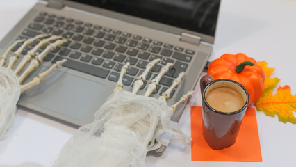 Skeleton Hands Typing on Laptop with Coffee Cup,Pumpikn, autumn leaves, Halloween Work Concept. side view