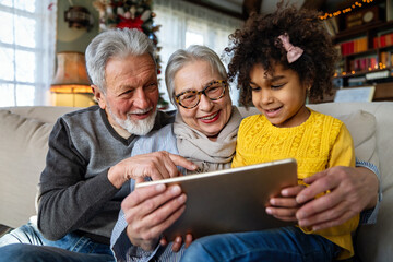 Mature couple with grandchild look at tablet screen and learn how to make video call or use laptop
