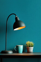 Desk lamp, cup and green potted plant on table near textured wall. Stylish home interior detail, minimal workspace