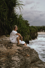 Man in white sitting on cliffside overlooking ocean waves