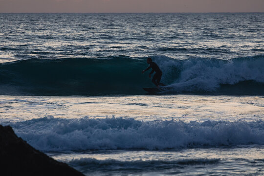 Surfer riding wave at sunset in algarve, portugal
